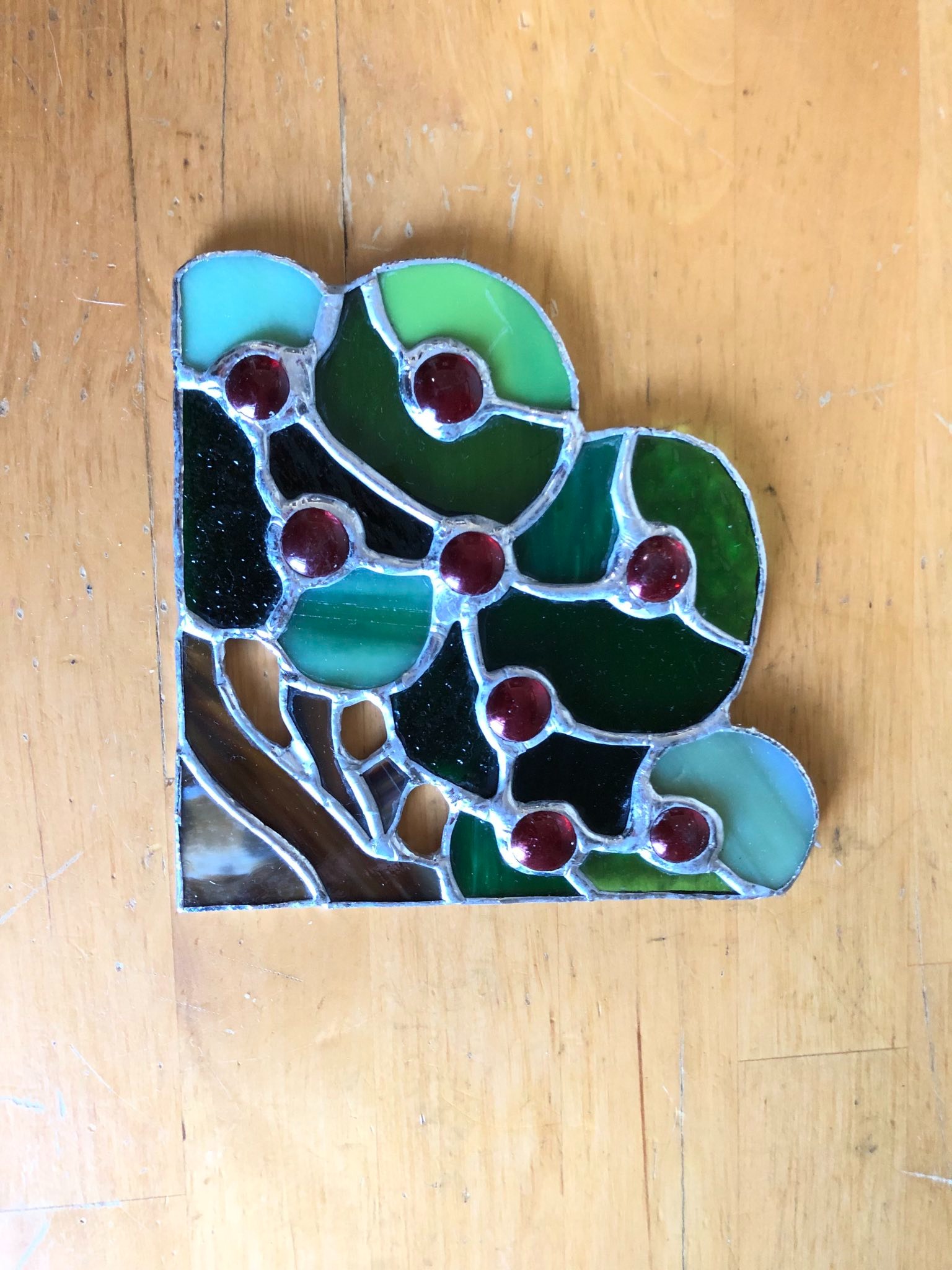 A stained glass bush with red berries that is laid on a table.