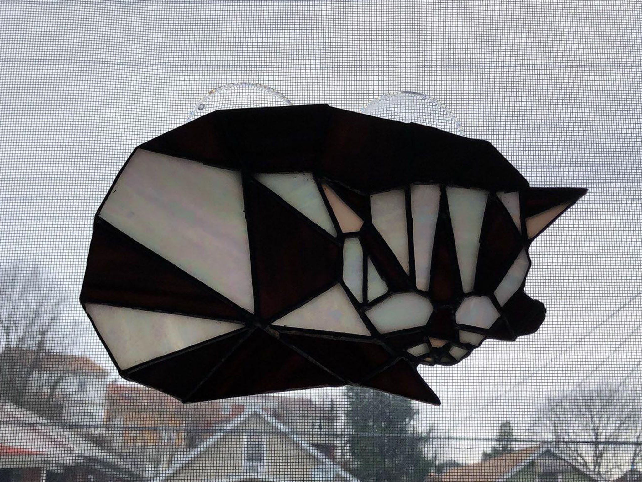 A stained glass cat that is hung on a window. The cat is largely made of triangles and gray and brown.