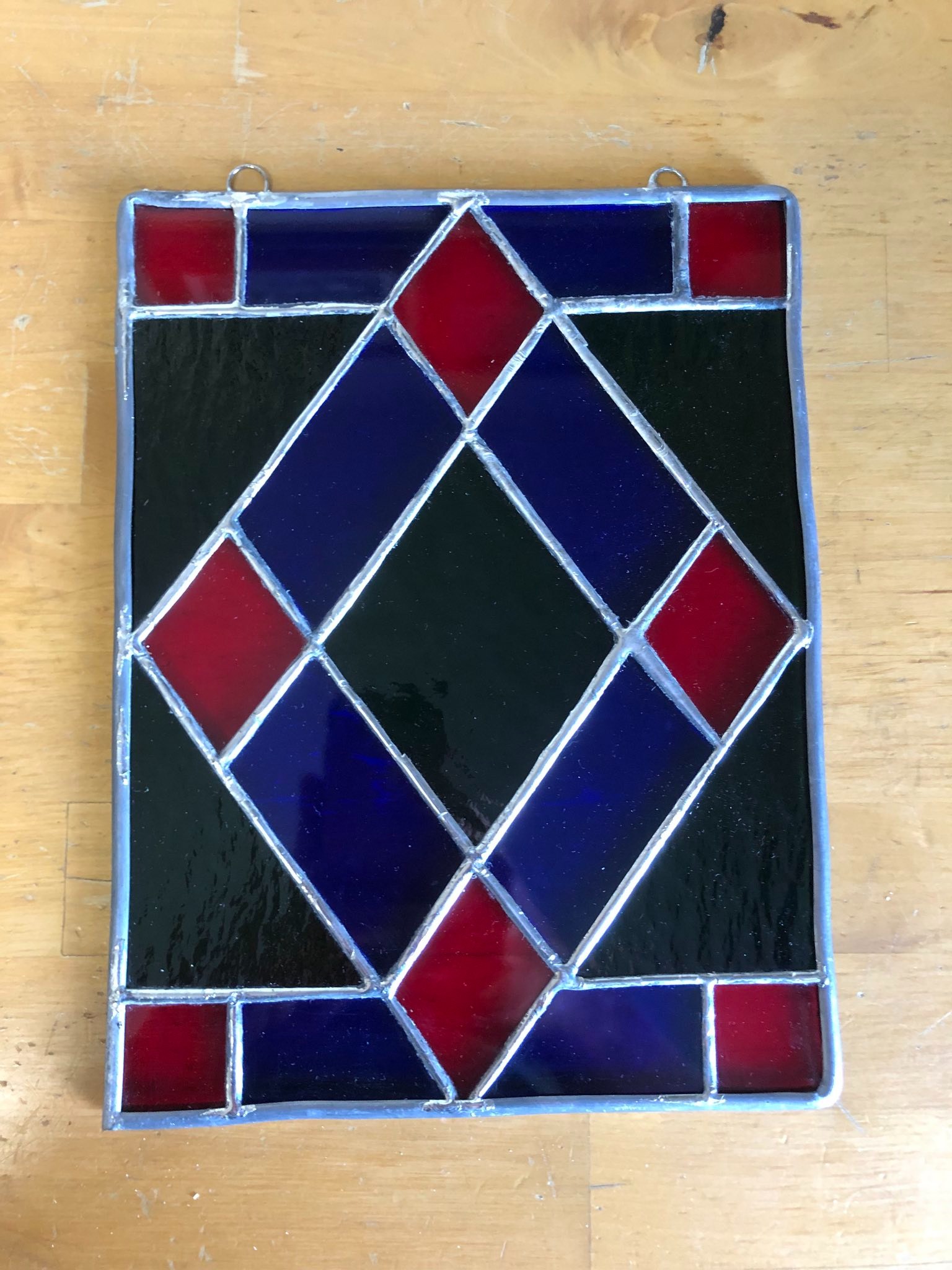 A stained glass geometric pattern that is laid on a table. In the center of the pattern is a diamond made of blue and red glass. The pattern also incorporates green glass behind the diamond.