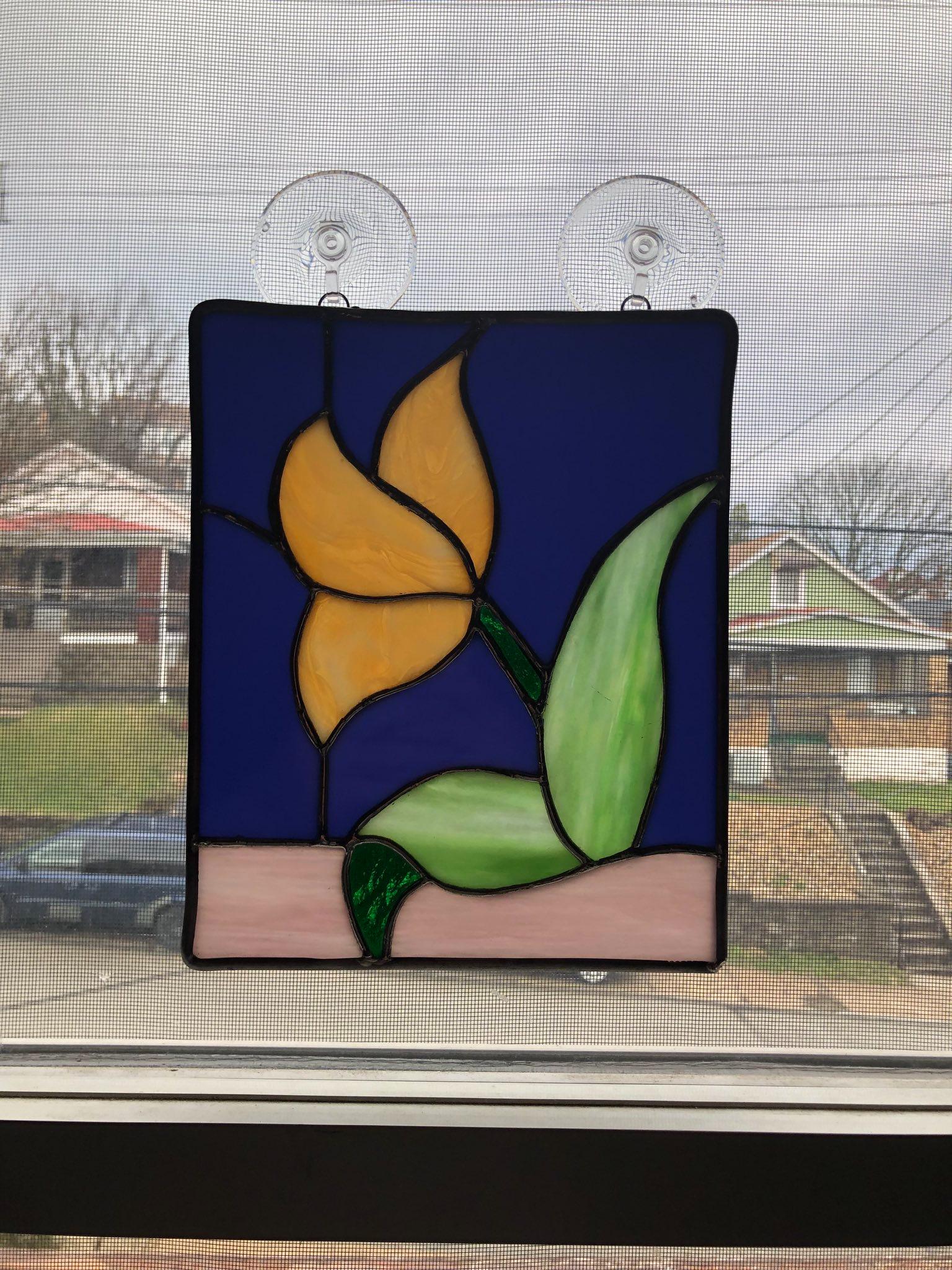 A stained glass panel that depicts a cream-colored flower on a blue background. The panel is hung on a window.