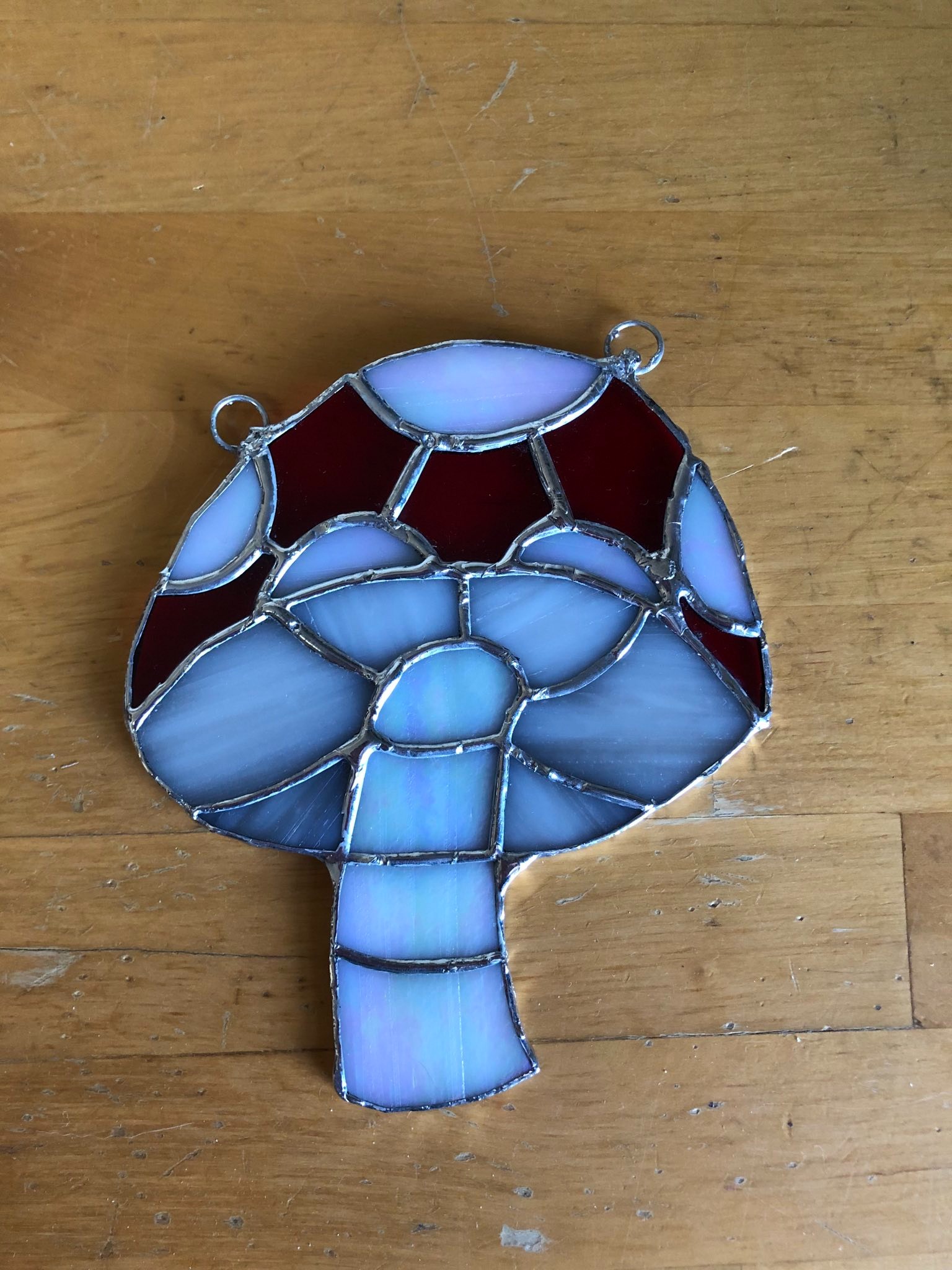 A stained glass mushroom that is laid on a table. The mushroom has a white stalk, red cap, and white spots.