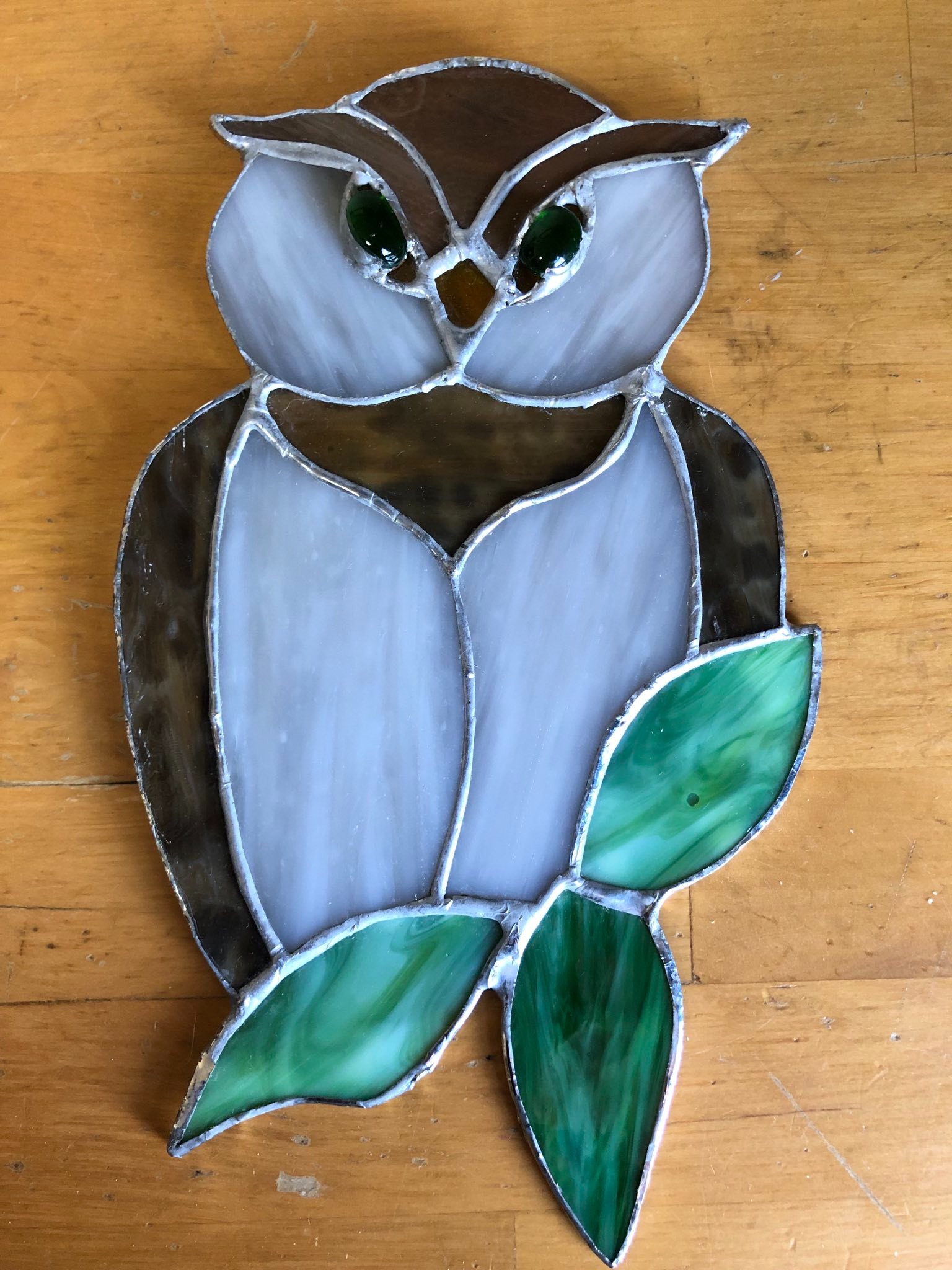 A stained glass owl that is perched on three leaves. The piece is laid on a table.